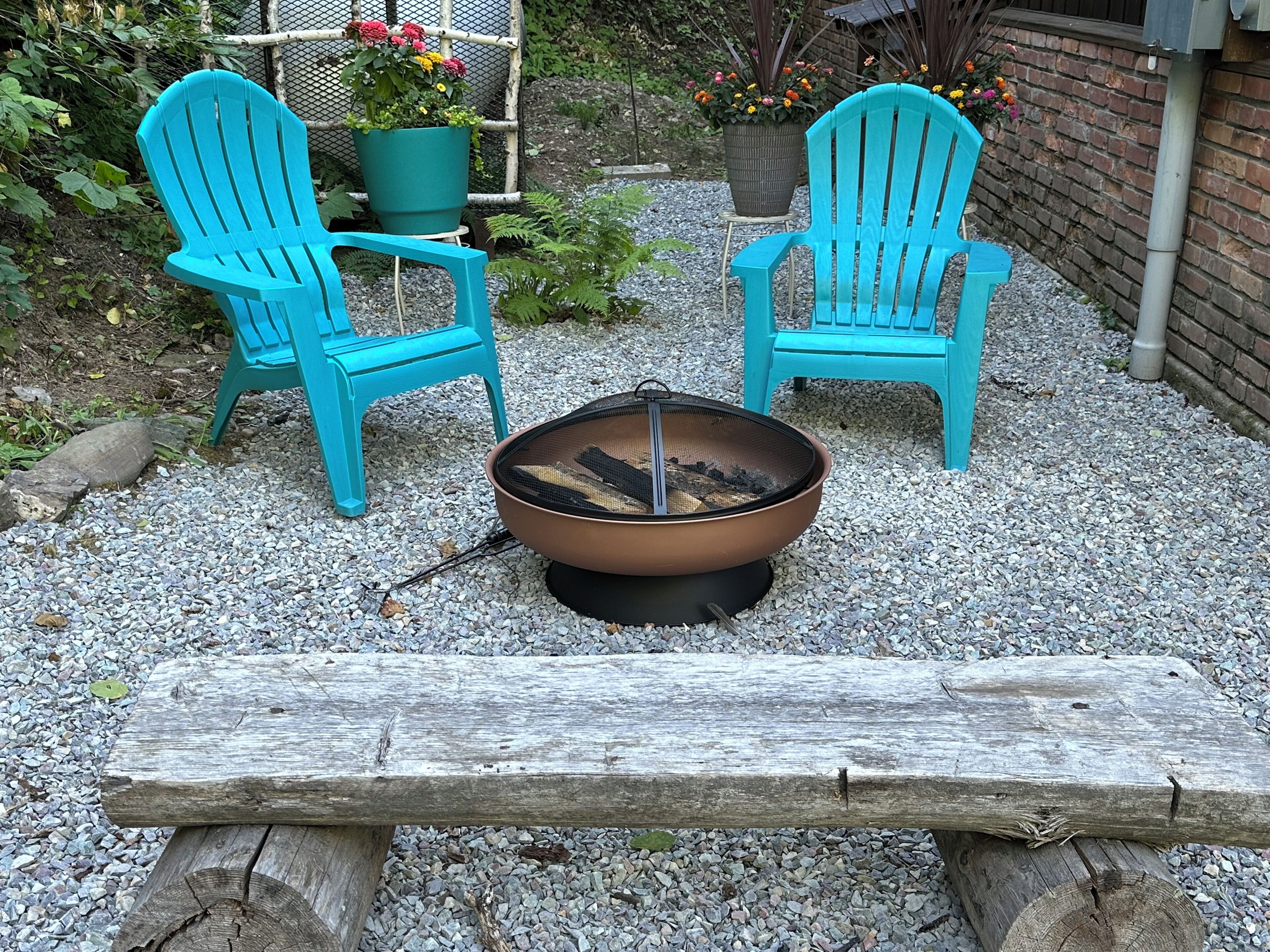 Two turquoise Adirondack chairs, a metal fire pit with logs, and a wooden bench.
