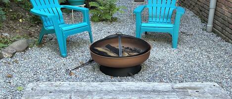 Two turquoise Adirondack chairs, a metal fire pit with logs, and a wooden bench.