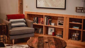Un salon chaleureux avec un fauteuil gris, une table basse en bois et une bibliothèque remplie de livres et de photos encadrées.
