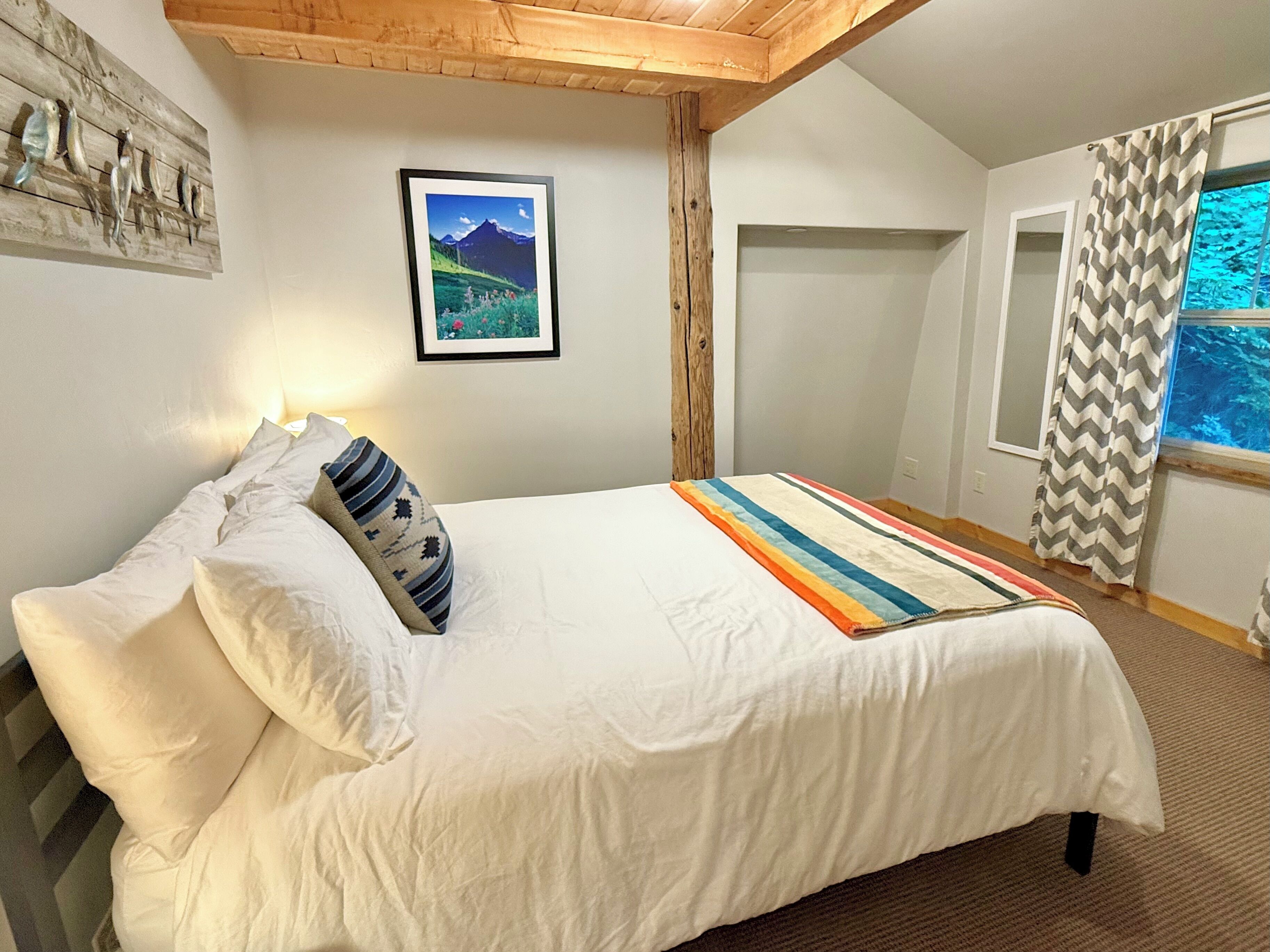 A bedroom with a bed, pillows, a framed picture, and a window with curtains.