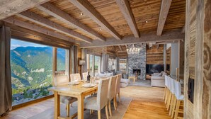 Un vaste espace de vie doté d’un plafond en bois, d’une cheminée en pierre et d’une grande fenêtre donnant sur un paysage montagneux.