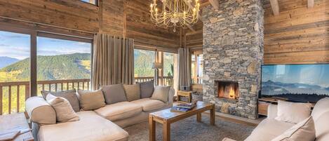 Un salón acogedor con chimenea de piedra, un televisor grande y una vista panorámica a las montañas.