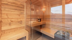 Un sauna aux murs en bois et doté d’une paroi en verre, avec un banc, une serviette et un seau contenant une brosse.