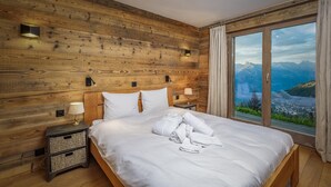 Une chambre avec un mur en bois, un grand lit, deux lampes de chevet et une vue sur les montagnes par une grande fenêtre.