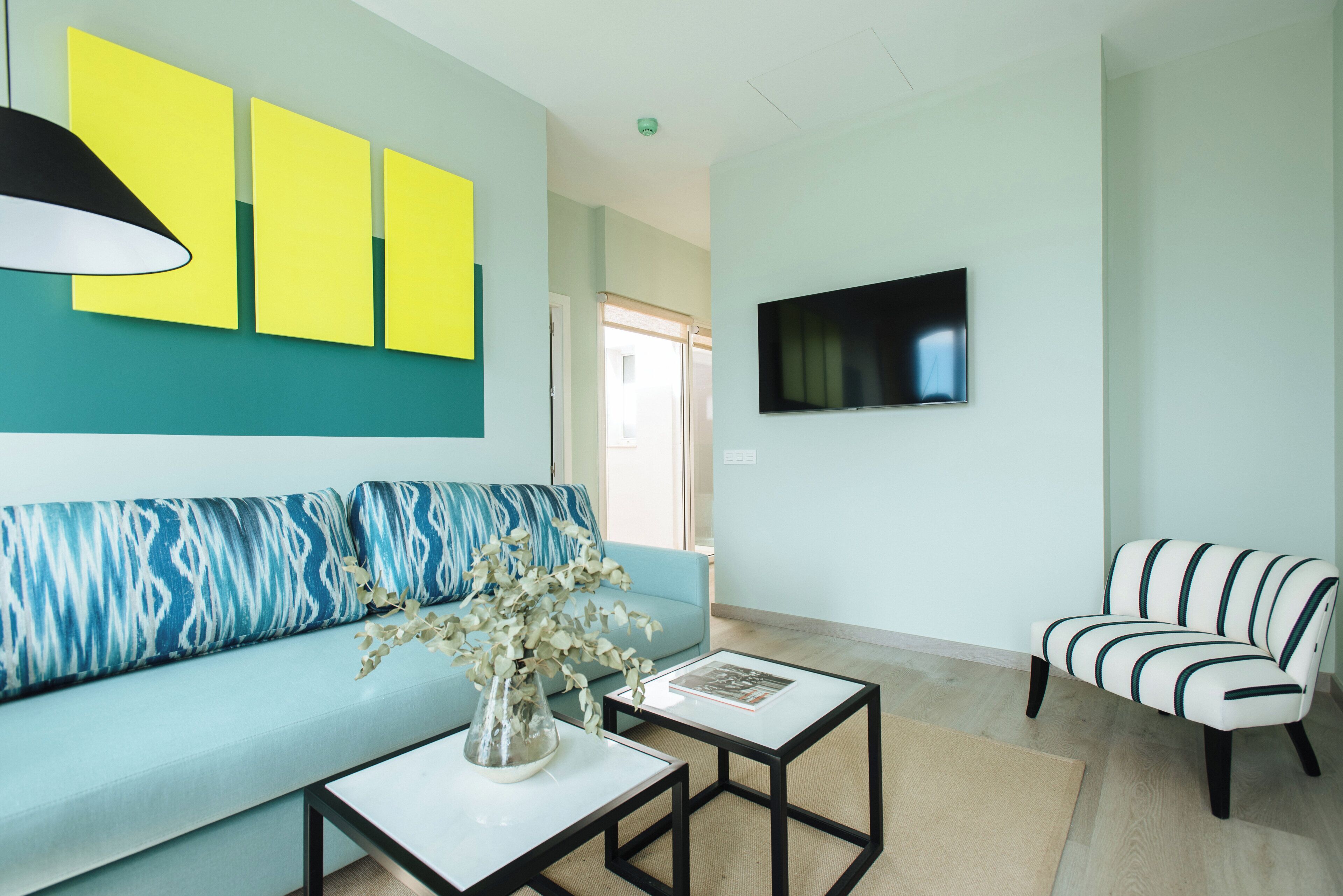 A modern living room with a light blue sofa, a striped armchair, a coffee table, and a flat-screen TV mounted on the wall.