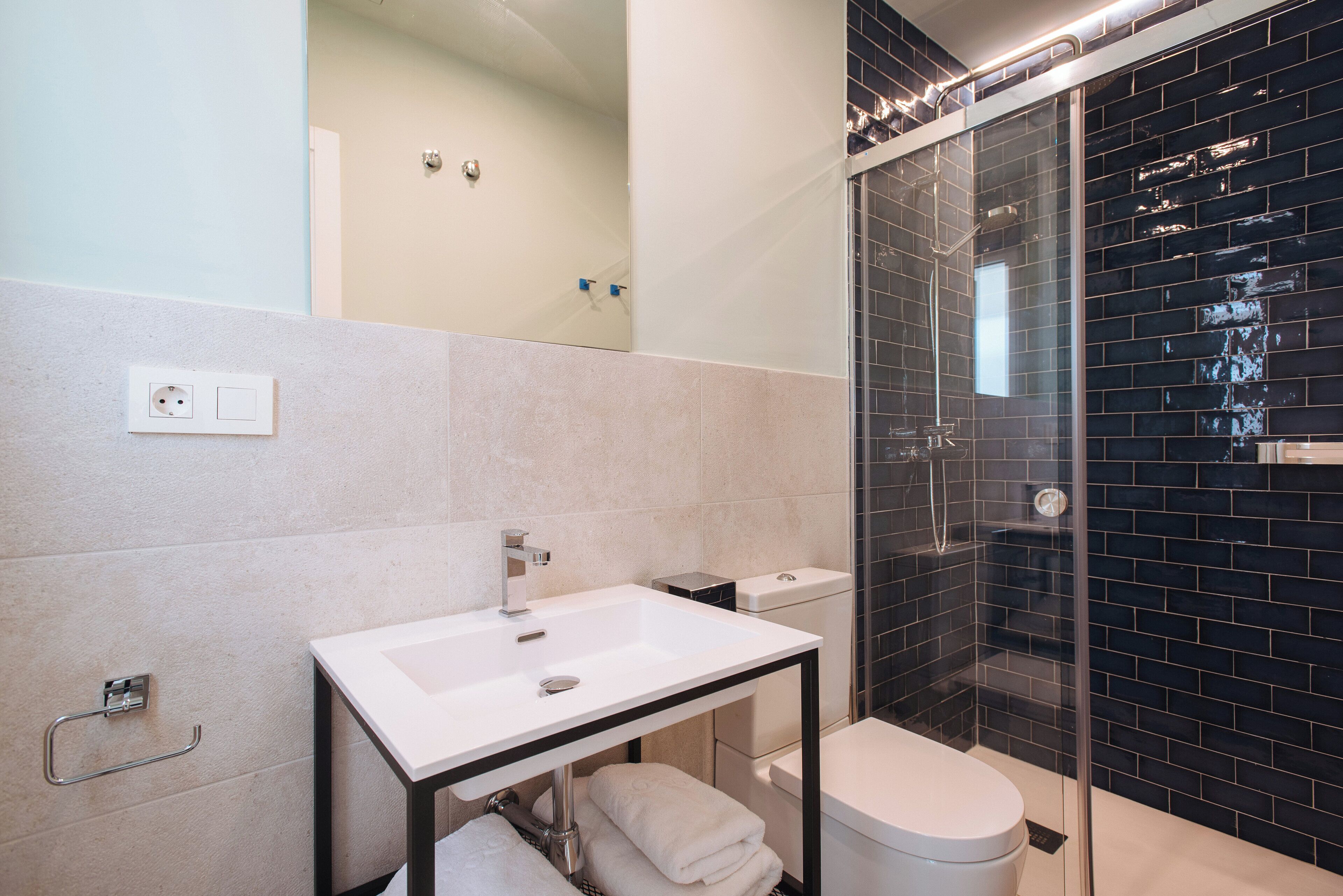 A modern bathroom with a white sink, black tiled shower, and a glass-enclosed shower area.