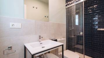 A modern bathroom with a white sink, black tiled shower, and a glass-enclosed shower area.