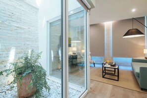 A modern living room with a glass wall, a potted plant, a sofa, a coffee table, and a hanging light fixture.