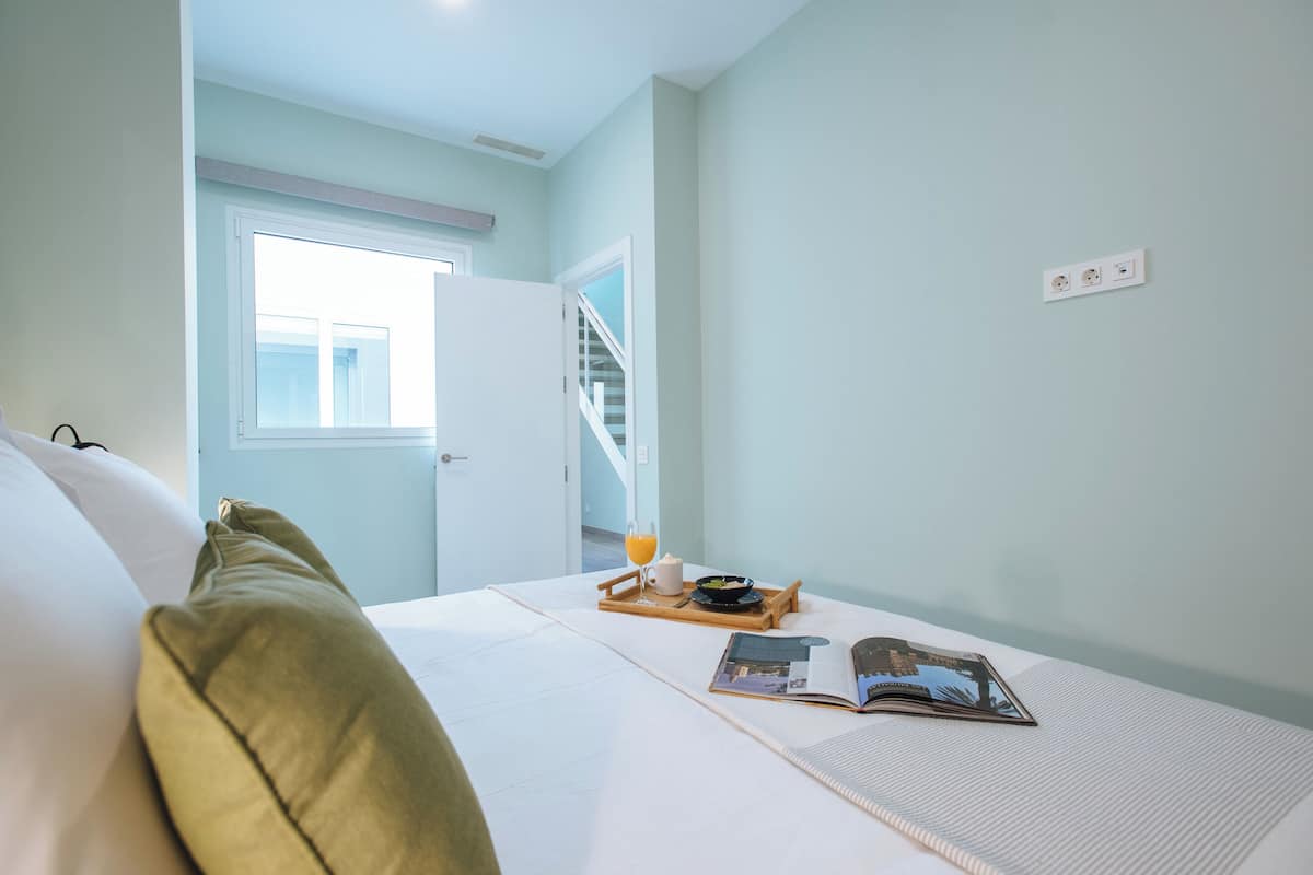 Ein Schlafzimmer mit Bett, Fenster, Tür und einem Frühstücksbrett mit Buch und Kaffeetasse.
