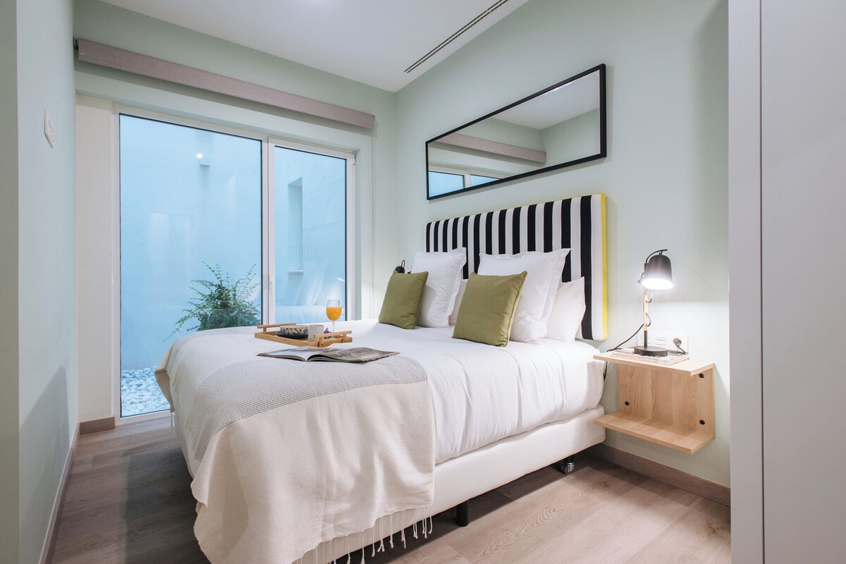 Una camera da letto con un letto grande, un comodino con una lampada, una finestra con vista e uno specchio sulla parete.