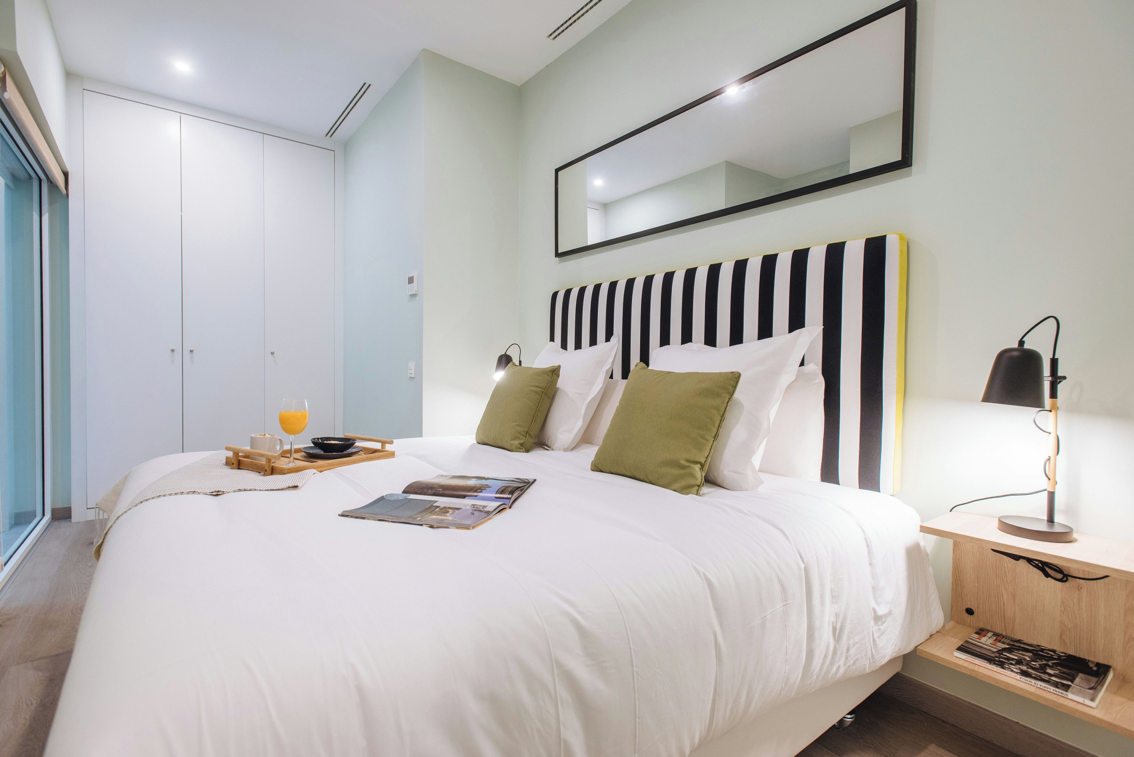 Un dormitorio moderno con una cama grande, mesitas de noche, un espejo y una ventana.