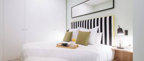 A neatly made bed with a tray of breakfast items, a bedside table with a lamp, and a large mirror on the wall.