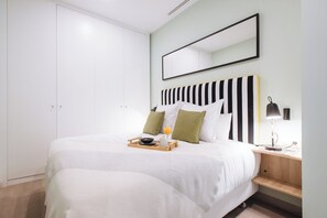 Ein ordentlich bezogenes Bett mit einem Tablett mit Frühstücksgegenständen, ein Nachttisch mit Lampe und ein großer Spiegel an der Wand.