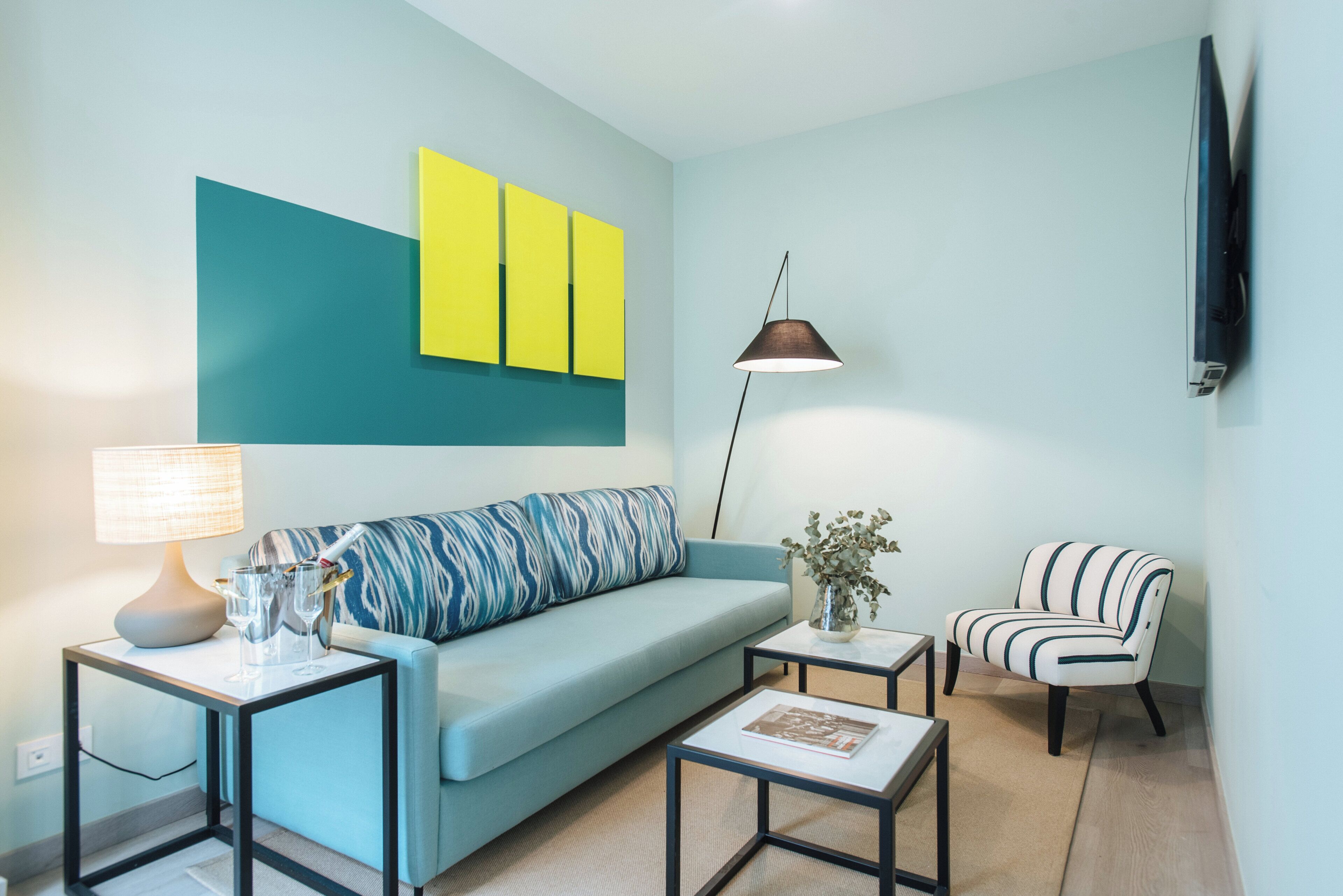 En moderne stue med en lyseblå sofa, en stribet lænestol, et lille sofabord og en gulvlampe.