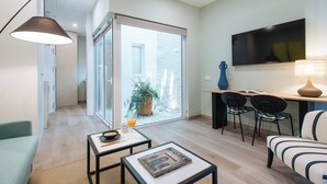 Een moderne woonkamer met een bank, een salontafel, een eethoek met stoelen, een televisie en een schuifpui naar een balkon met een plant in pot.