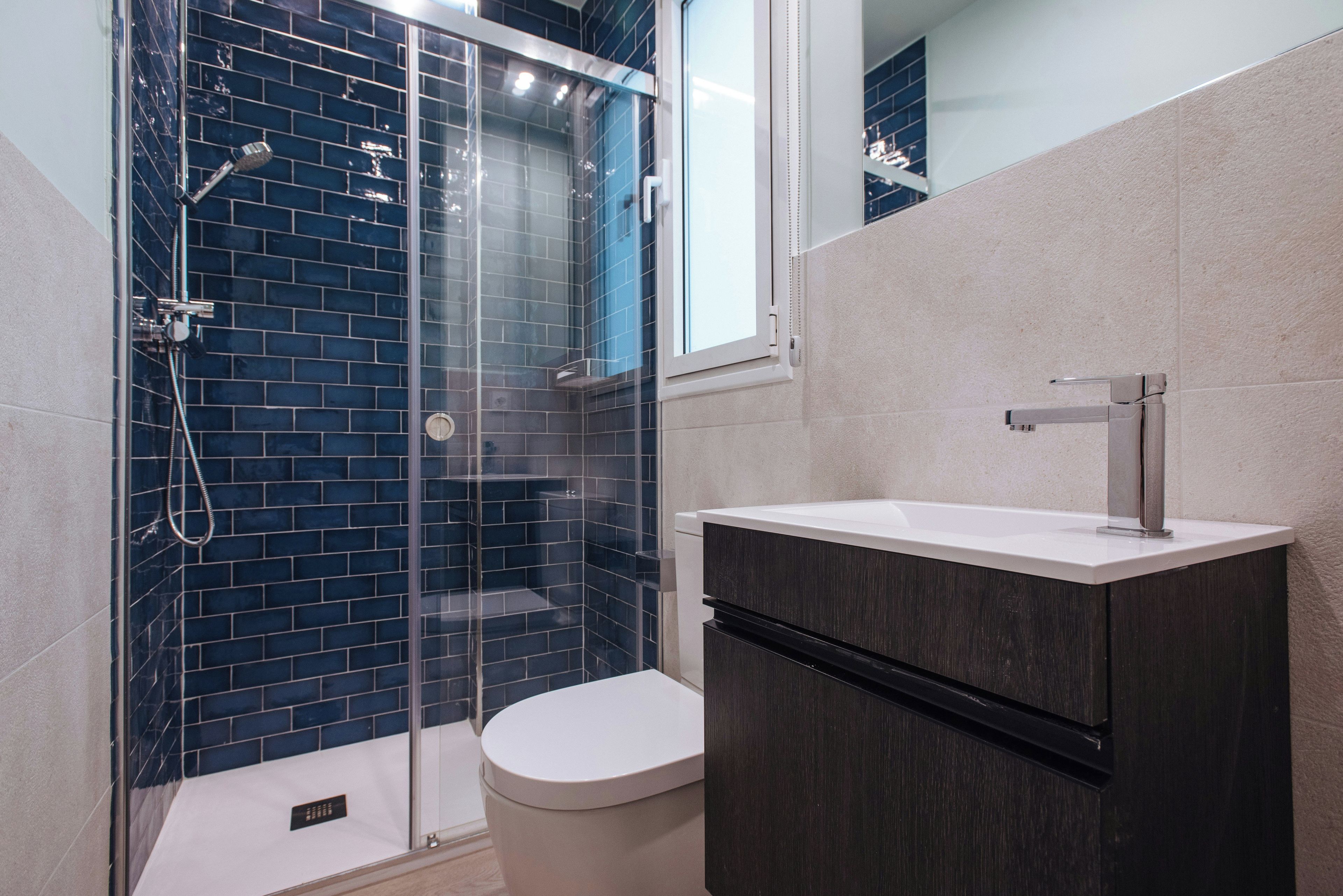 Un baño moderno con ducha de vidrio, inodoro blanco y mueble de madera oscura.