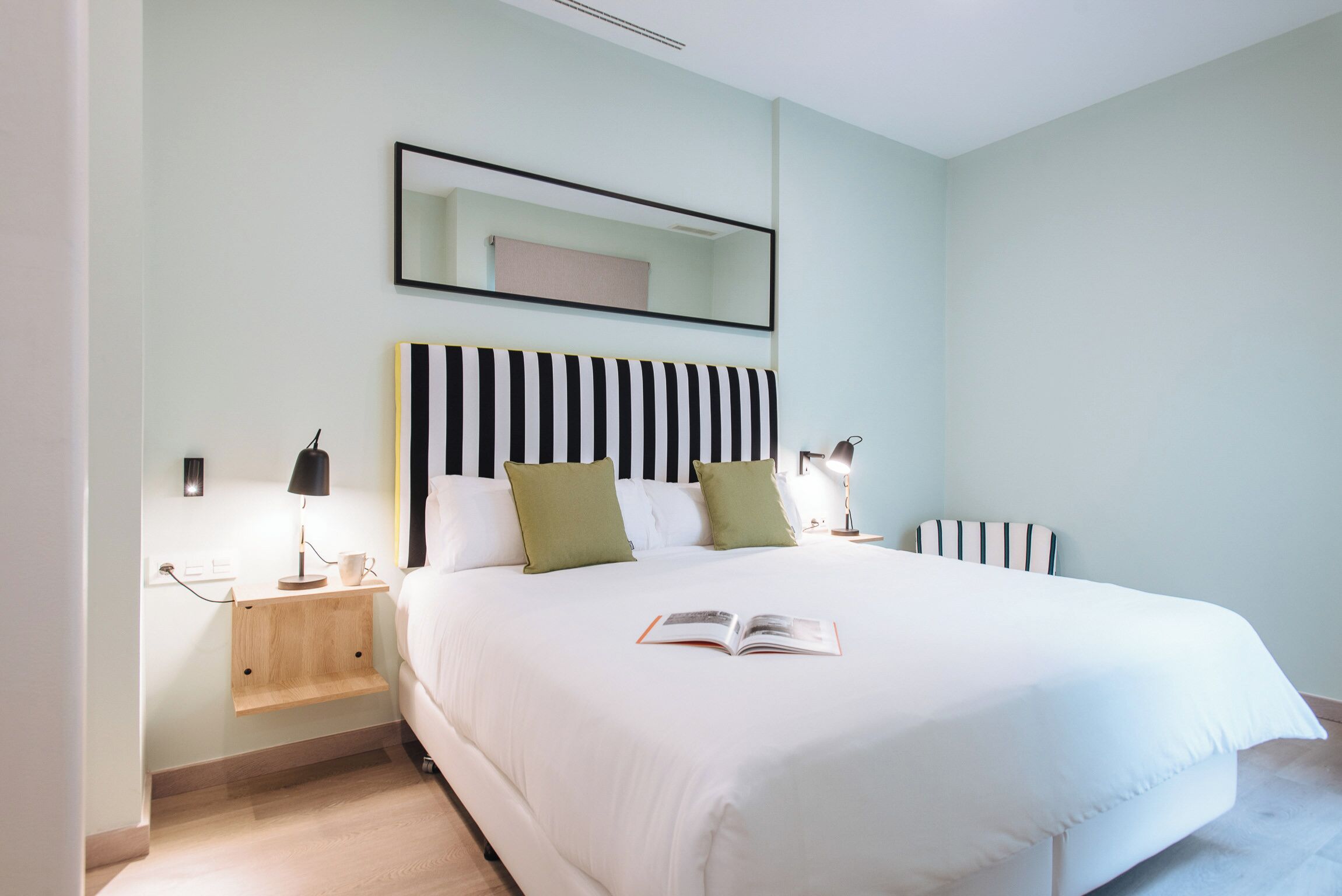 A neatly arranged bedroom with a large bed, bedside tables, a mirror, and a book on the bed.