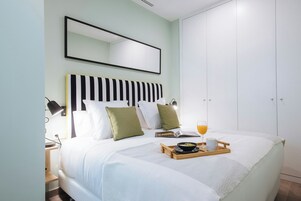 A neatly made bed with pillows, a bedside lamp, a tray with breakfast items, and a book.