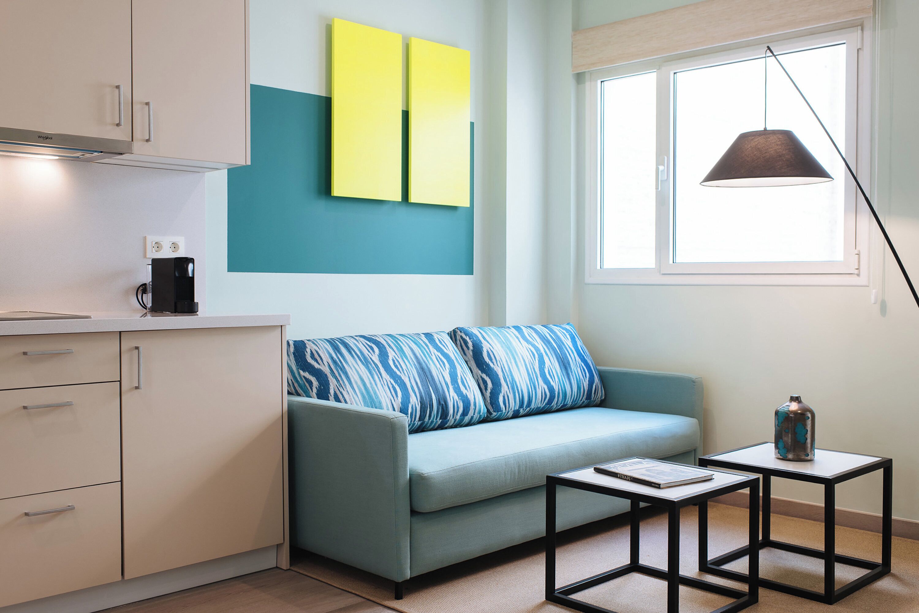 Una sala de estar moderna con un sofá, una cafetera, una mesa y un ventanal con una lámpara colgante.