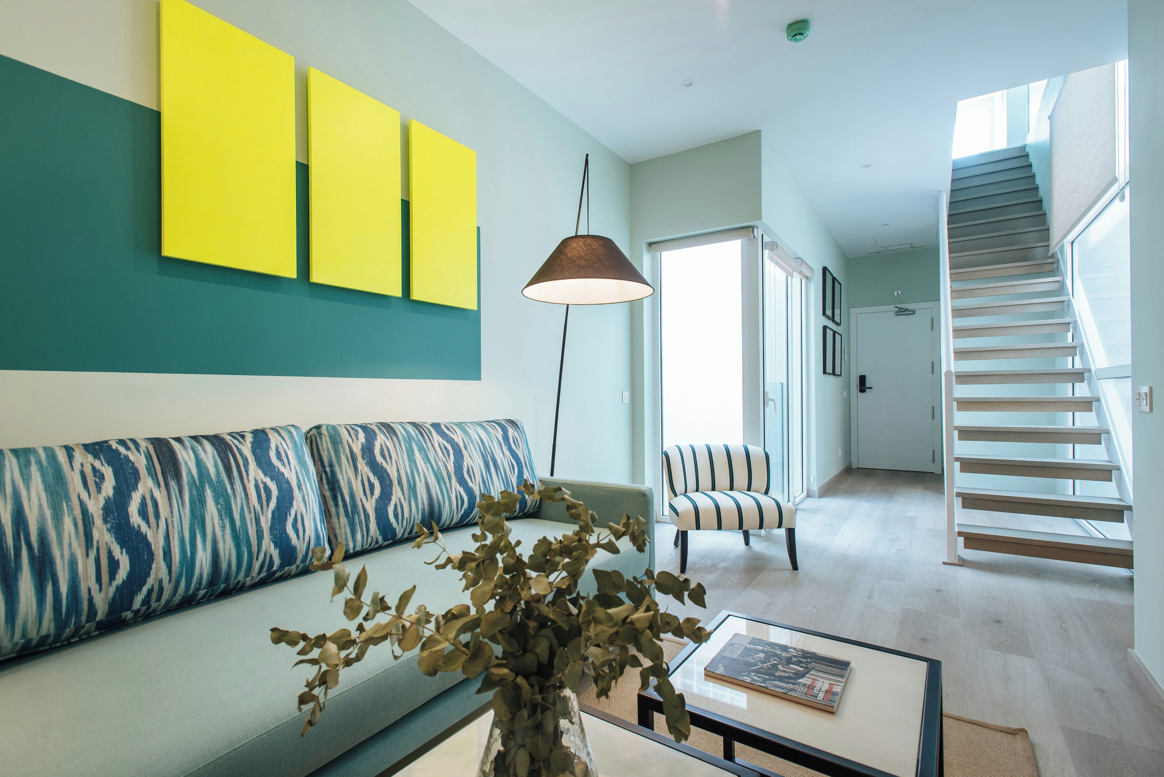 Un salon moderne avec un canapé, une table basse sur laquelle repose un livre, une lampe et un escalier menant à un autre niveau.