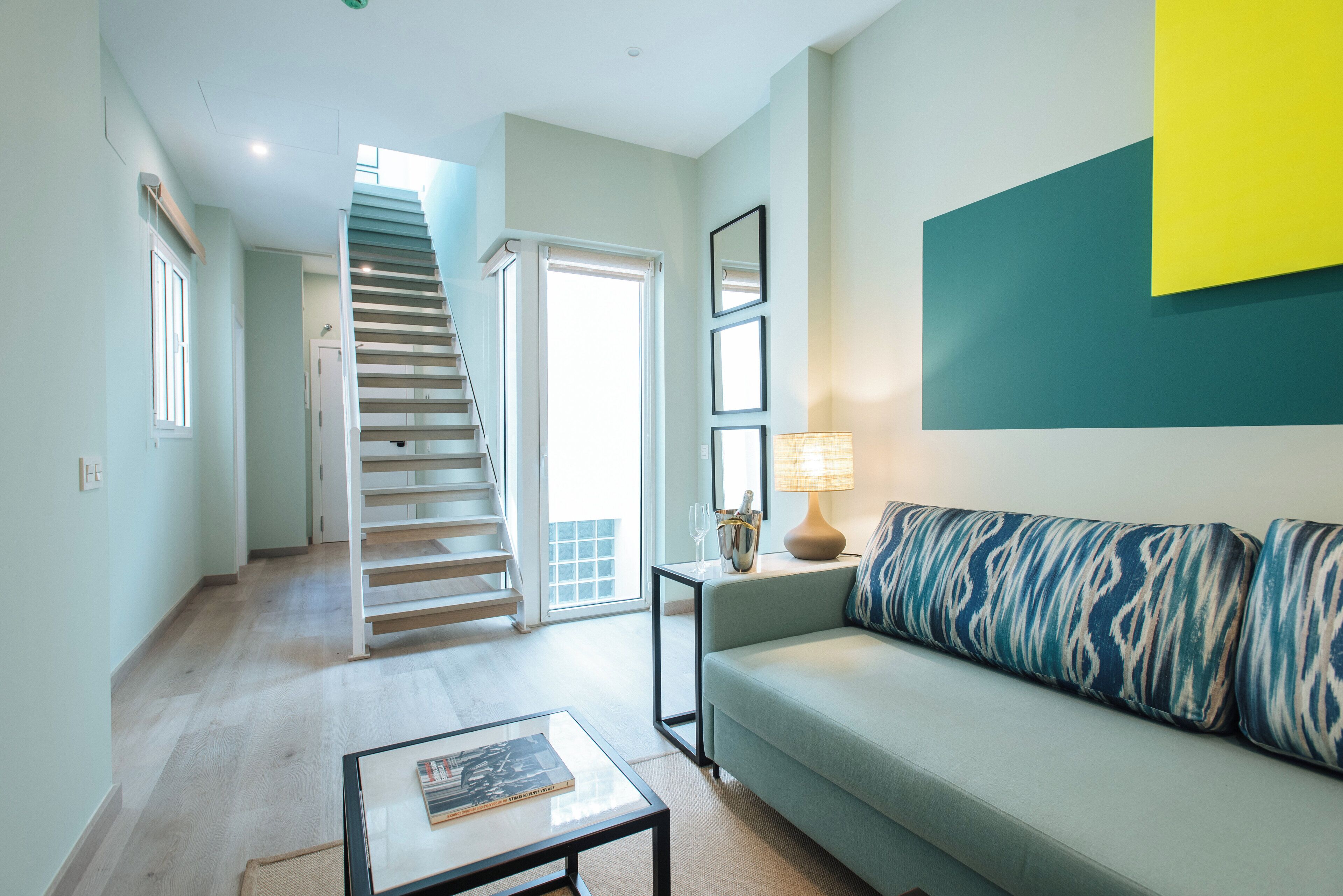 A modern living room with a staircase, a sofa, a coffee table, and a lamp.