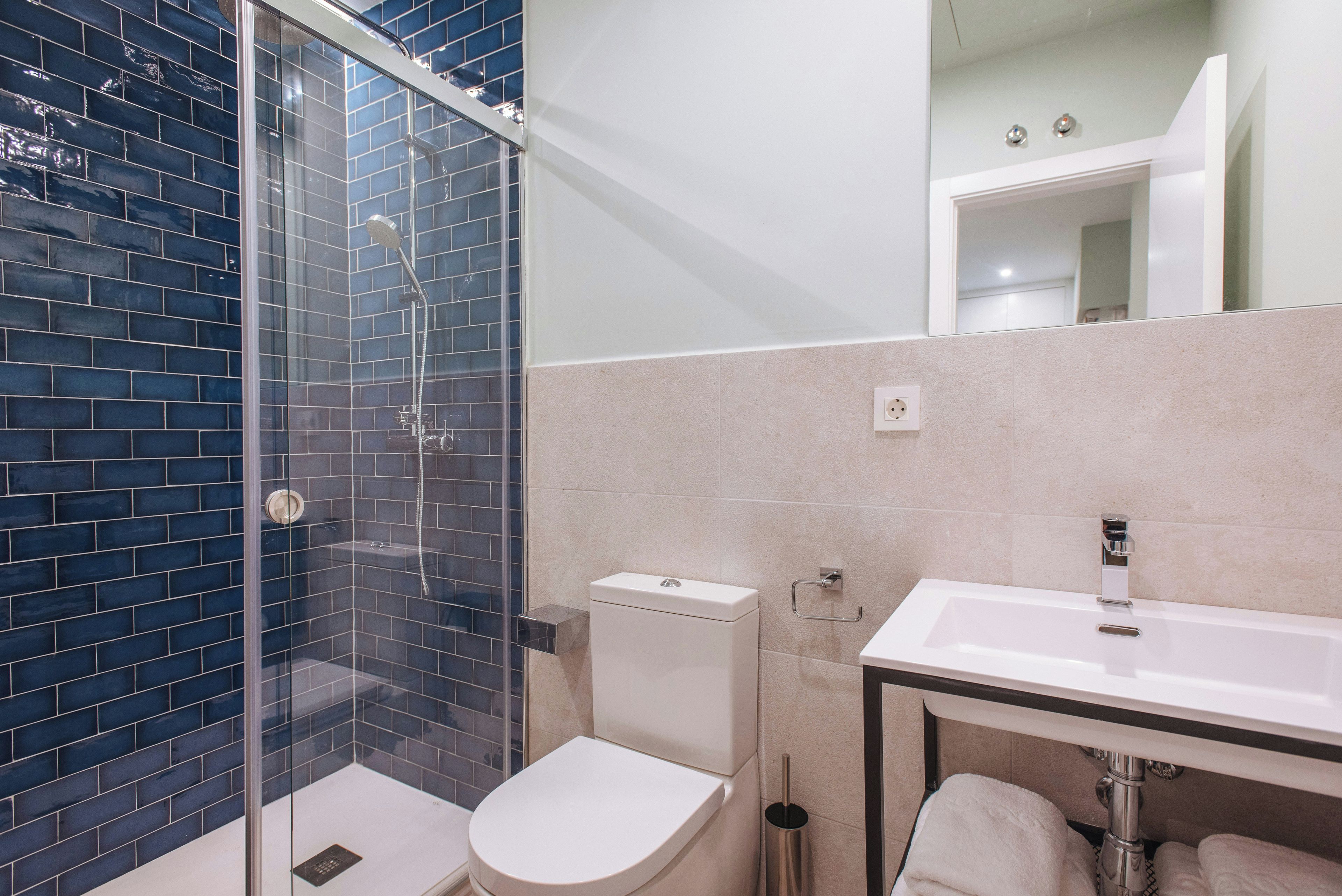 Un bany modern amb dutxa d'acer, un vàter blanc i un lavabo amb mirall a la part superior.