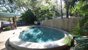 Una piscina con una valla de madera y un área cubierta con un banco.