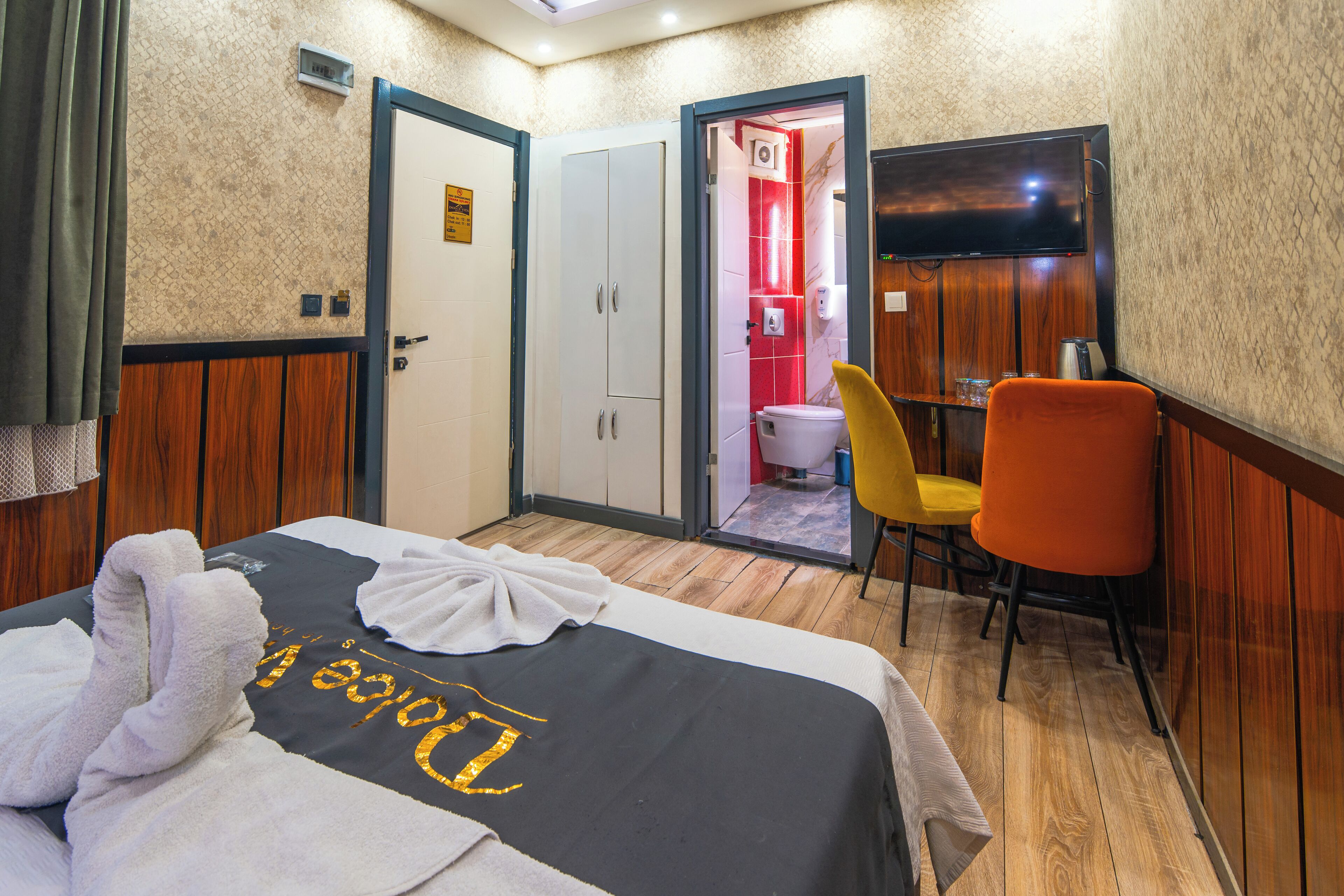 Une chambre d’hôtel avec un lit, un bureau, une chaise, une télévision et une salle de bain visible à travers une porte ouverte.