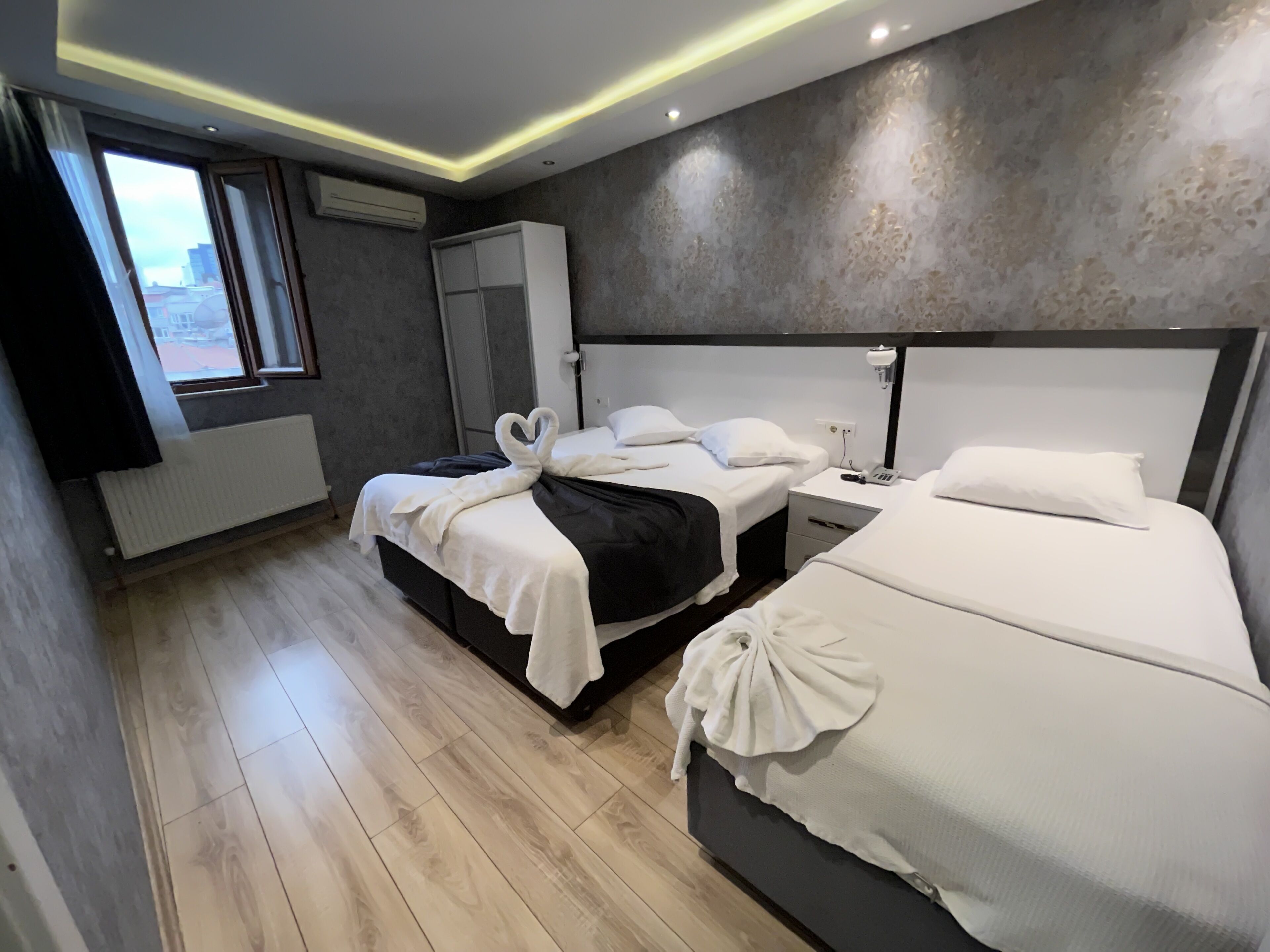 A modern hotel room with two beds, a wardrobe, a radiator, and a window with a view.