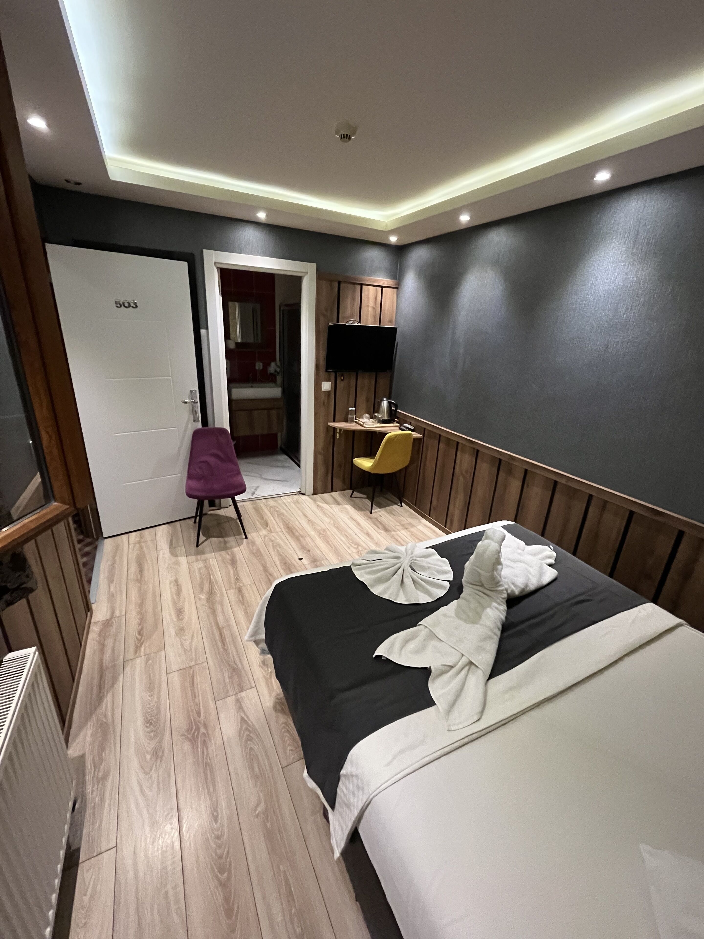 A hotel room with a bed, a desk, a television, and a bathroom visible through an open door.