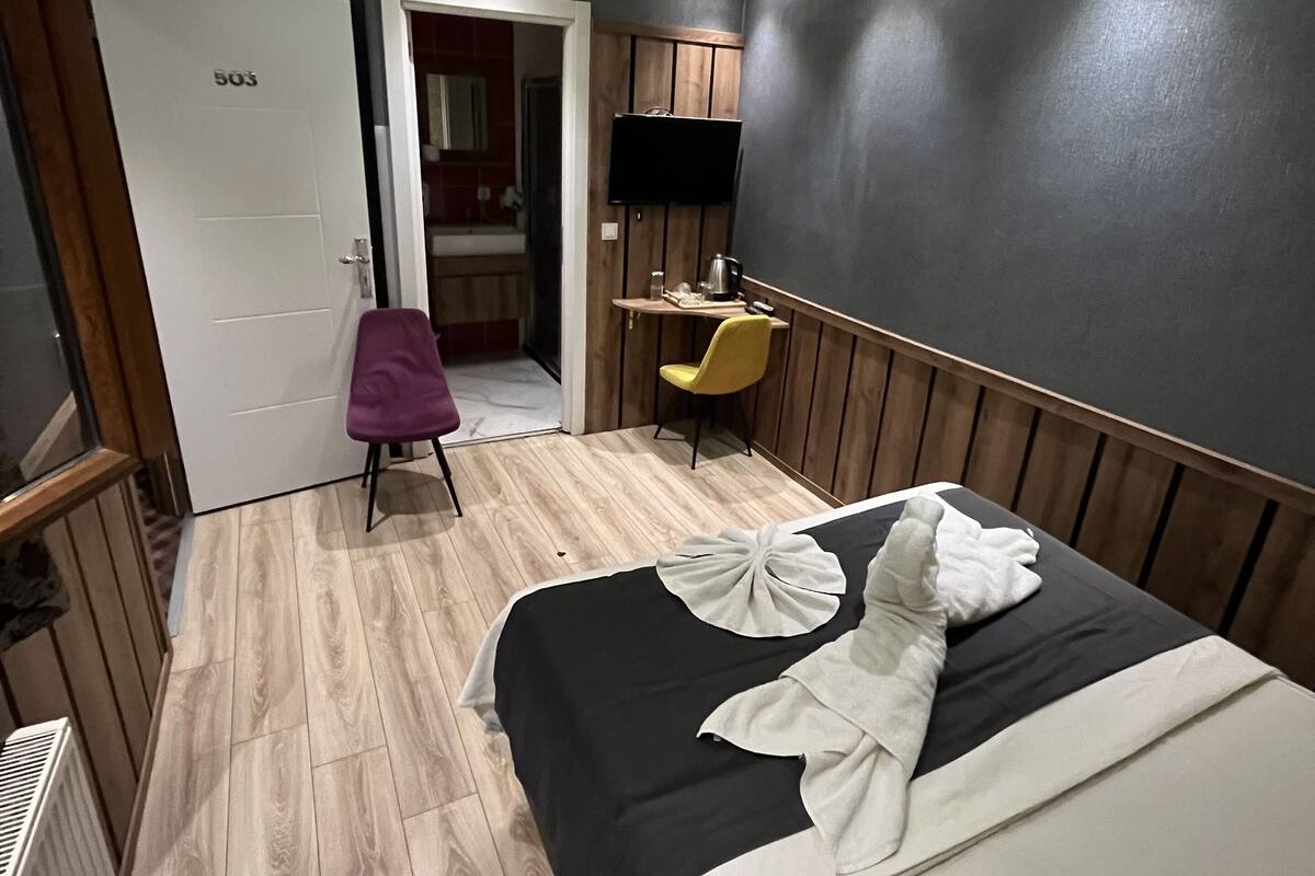 A hotel room with a bed, a desk, a television, and a bathroom visible through an open door.