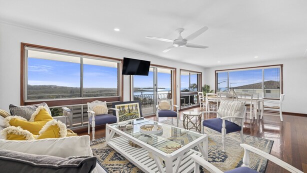 A spacious living area with large windows, a ceiling fan, and a glass coffee table.