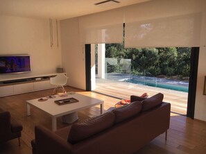 A modern living room with a large window, a flat-screen TV, a white coffee table, and a brown sofa.