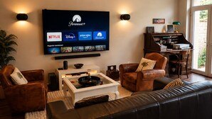 Ein modernes Wohnzimmer mit großem Flachbildfernseher, Ledersofas, einem Couchtisch und einem Bücherregal.