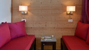 A room with two red sofas, a small table with a magazine, and two wall-mounted lamps.