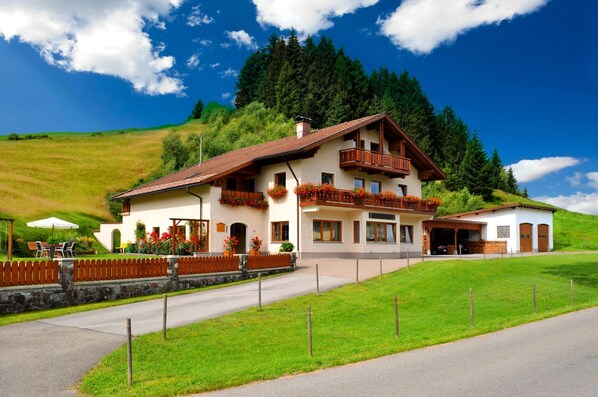 A two-story chalet with a balcony, a covered patio, and a mountain backdrop. - Bergquell Tirol (Jungholz)