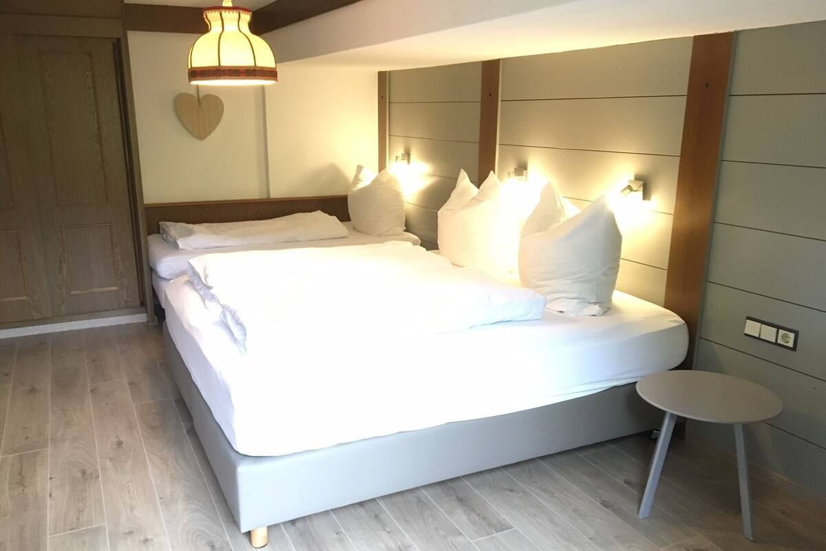 A neatly made bed with white linens and pillows, a bedside table, and a hanging light fixture.