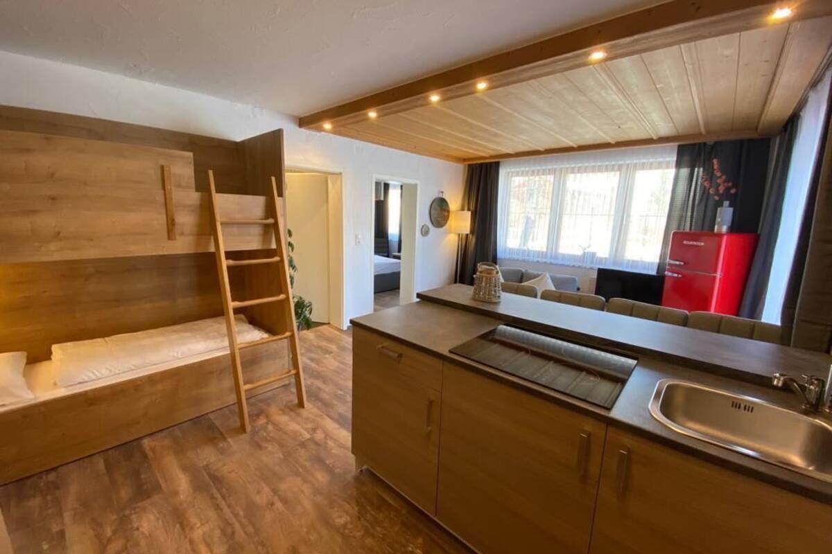 A compact kitchen with wooden cabinetry, a built-in bench with a ladder, a sink, and a red appliance.