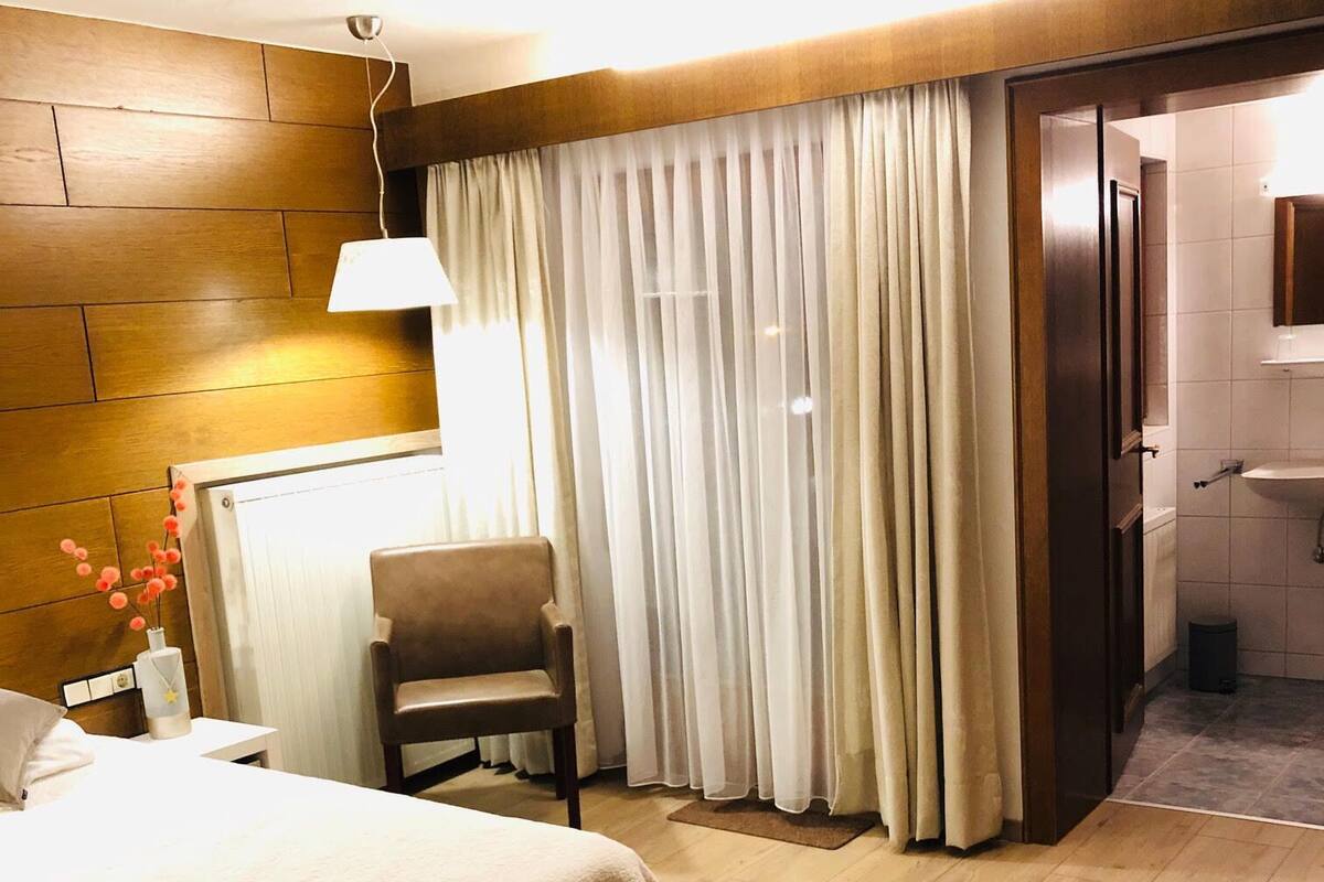 A hotel room with a large bed, a chair, a desk, a lamp, and a bathroom visible through an open door.