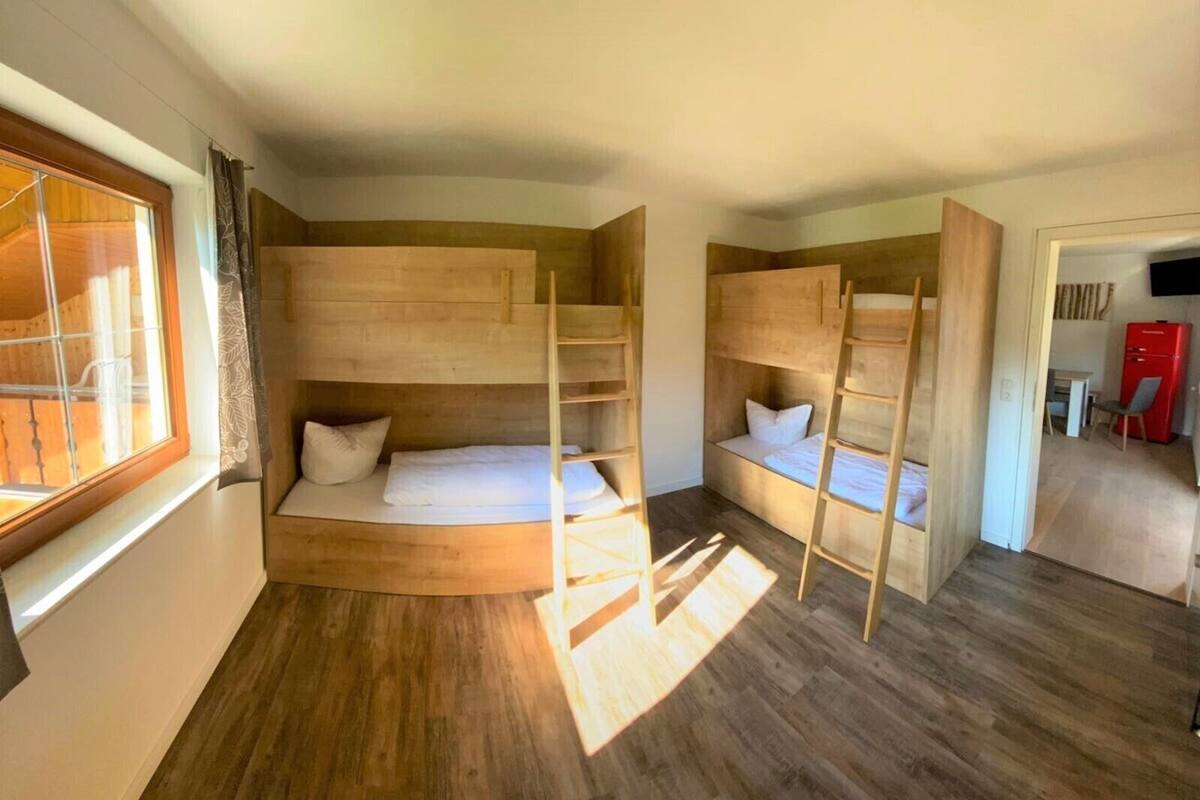 A room with bunk beds, a window, a red refrigerator, and a wooden floor.