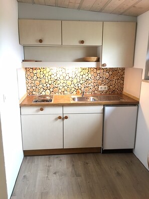 A compact kitchen with white cabinets, a wooden countertop, and a backsplash made of stacked logs. - Bergquell Tirol (Jungholz)