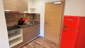 Una cocina compacta con un armario de madera, un refrigerador rojo y una cafetera.