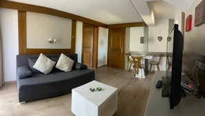 Una sala de estar moderna con un sofá gris, una mesa de centro blanca y un comedor con sillas de madera y una mesa.