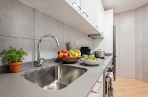 Uma cozinha moderna com uma pia de aço inoxidável, uma fruteira, uma saladeira, uma cafeteira e um vaso com planta.