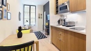 A compact kitchen with modern appliances, a dining area with a table and chairs, and a visible window with blinds. - Blanche 1 - Studio Apartment, Sleeps 2 (Paris)