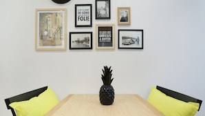 A dining table with a pineapple centerpiece, surrounded by chairs with yellow cushions, and framed pictures on the wall above. - Blanche 1 - Studio Apartment, Sleeps 2 (Paris)