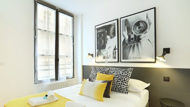 A hotel room with a bed, a small round table, and two framed pictures on the wall. - Blanche 1 - Studio Apartment, Sleeps 2 (Paris)