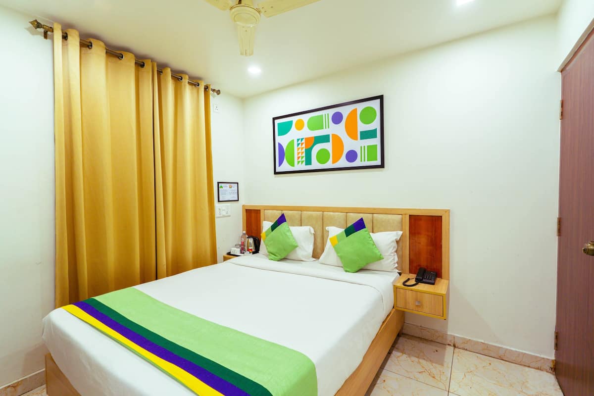 A hotel room with a bed, a nightstand, a telephone, a framed picture on the wall, and a curtain.