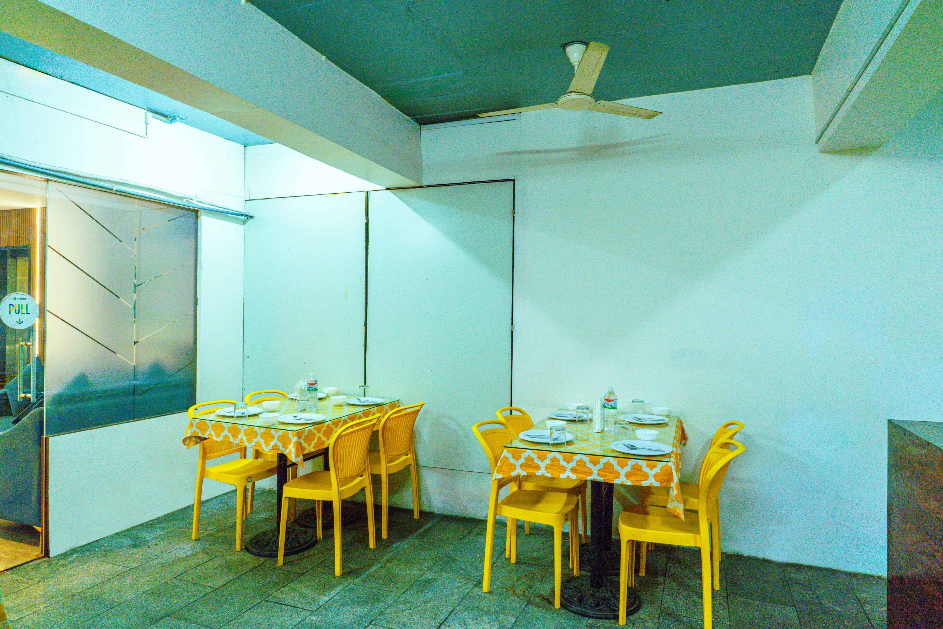 Zona pranzo con due tavoli, sedie gialle e una ventola a soffitto.
