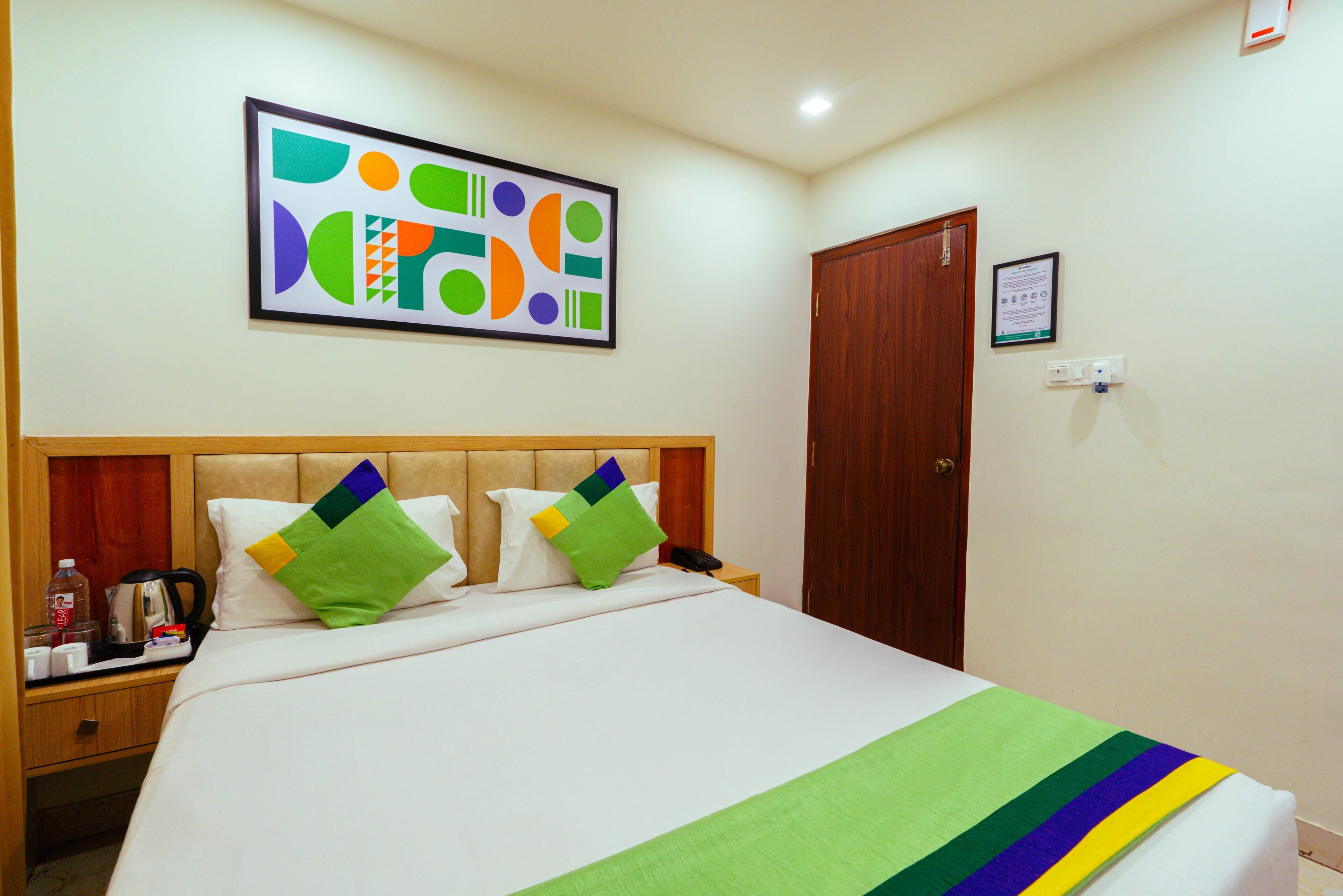 A hotel room with a large bed, a wooden headboard, and a colorful abstract painting on the wall.